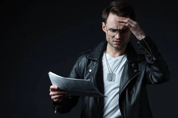 Besorgter brutaler Mann in Biker-Jacke mit Zeitung auf Schwarz — Stockfoto