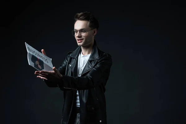 Stylish brutal man in biker jacket with business newspaper isolated on black — Stock Photo