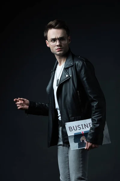 Serious stylish brutal man in biker jacket with business newspaper isolated on black — Stock Photo