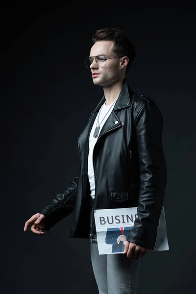 Side view of stylish brutal man in biker jacket with business newspaper isolated on black — Stock Photo