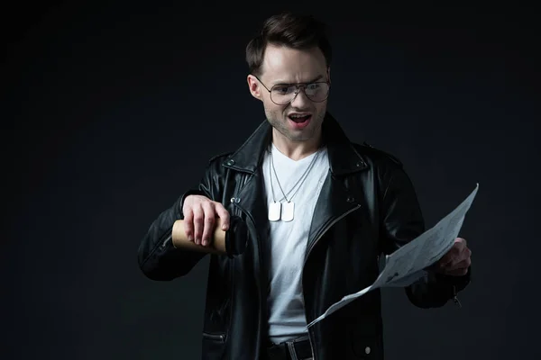 Schockierter brutaler Mann in Biker-Jacke mit Zeitung und Kaffee to go auf schwarz — Stockfoto