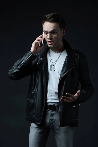 Scioccato uomo teso elegante in giacca di pelle parlando su smartphone isolato su nero — Foto stock