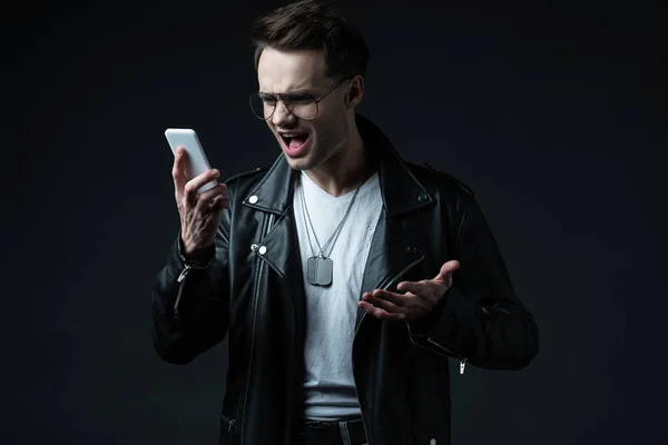 Angry stylish man in leather jacket yelling at smartphone isolated on black — Stock Photo