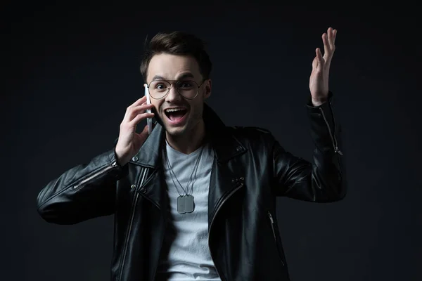 Happy excited stylish man in leather jacket talking on smartphone isolated on black — Stock Photo