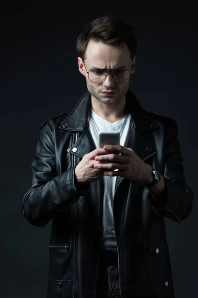 Besorgter Mann in Lederjacke nutzt Smartphone isoliert auf Schwarz — Stockfoto