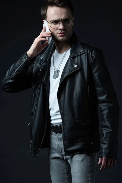 Tense stylish man in leather jacket talking on smartphone isolated on black — Stock Photo