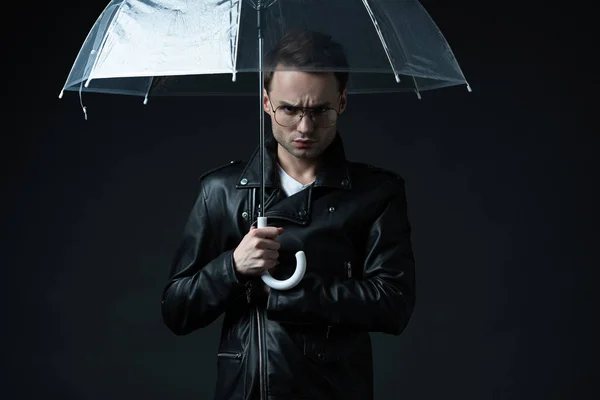 Angry stylish brutal man in biker jacket with umbrella isolated on black — Stock Photo