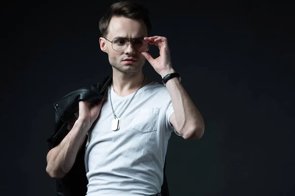 Hombre brutal elegante posando con chaqueta de ciclista y gafas aisladas en negro - foto de stock