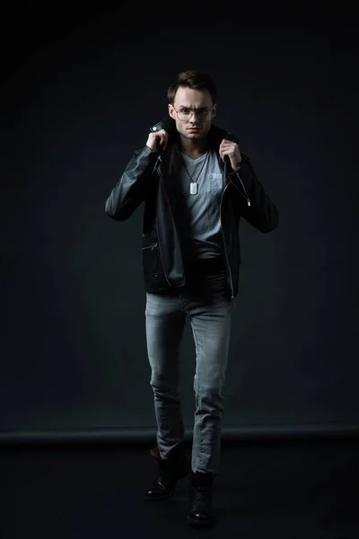 Stylish brutal man posing in biker jacket on black — Stock Photo