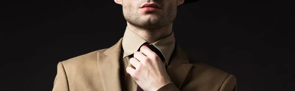 Vista recortada de hombre elegante en traje beige fijación corbata aislado en negro, tiro panorámico - foto de stock