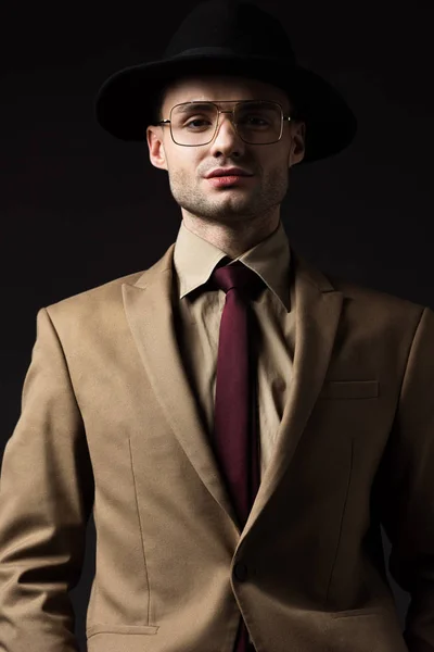 Homem elegante confiante em terno bege, chapéu e óculos isolados em preto — Fotografia de Stock