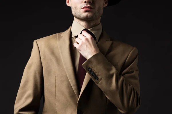 Corte vista de homem elegante em terno bege fixação laço isolado no preto — Fotografia de Stock