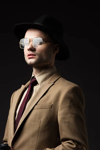 Élégant homme en costume beige, chapeau et lunettes isolé sur noir — Photo de stock