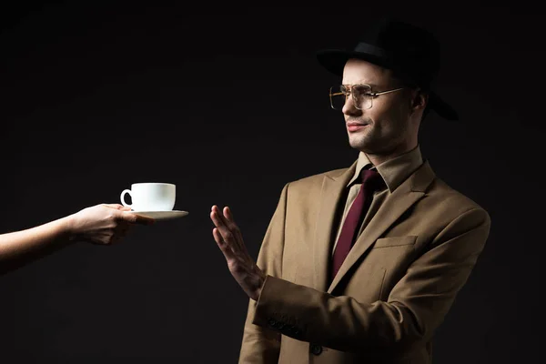 Élégant homme en costume beige, chapeau et lunettes refusant le café du serveur isolé sur noir — Photo de stock