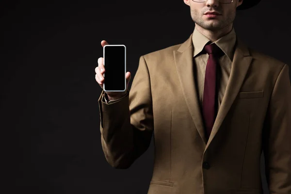 Vue recadrée de l'homme élégant en costume beige tenant smartphone avec écran blanc isolé sur noir — Photo de stock