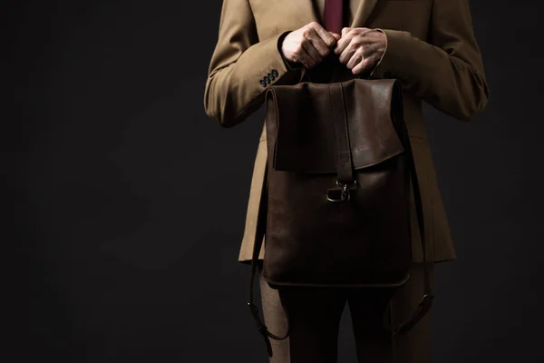 Vista recortada de hombre elegante en traje beige con mochila de cuero marrón aislado en negro - foto de stock