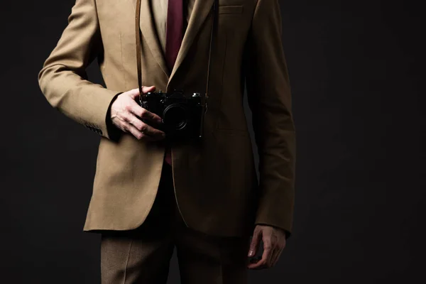 Cropped view of elegant man in beige suit, hat and eyeglasses with film camera isolated on black — Stock Photo