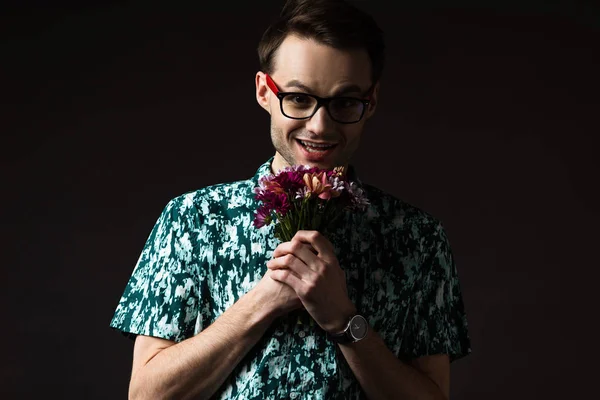 Excité homme à la mode dans les lunettes en chemise colorée bleue tenant bouquet floral isolé sur noir — Photo de stock