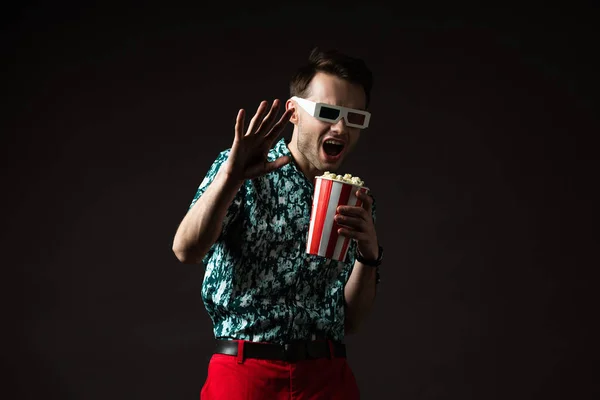 Verängstigter modischer Mann mit 3D-Brille in blauem, buntem Hemd und roter Hose, Popcorn isoliert auf schwarz haltend — Stockfoto