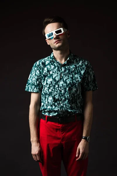 Fashionable man in 3d glasses in blue colorful shirt and red pants isolated on black — Stock Photo