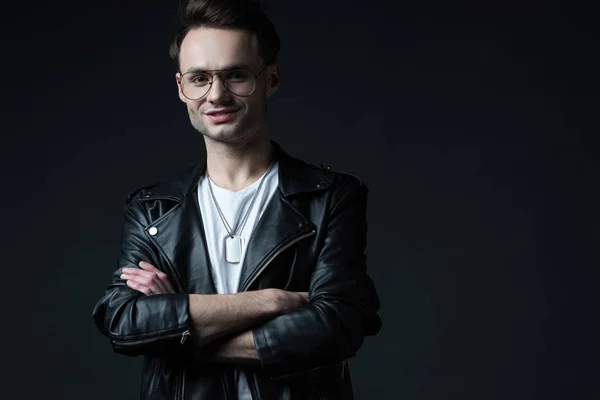 Smiling stylish brutal man in biker jacket with crossed arms isolated on black — Stock Photo