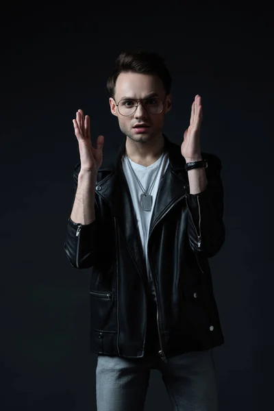 Worried stylish brutal man in biker jacket gesturing isolated on black — Stock Photo