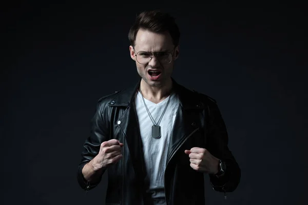 Angry stylish brutal man in biker jacket showing fists isolated on black — Stock Photo