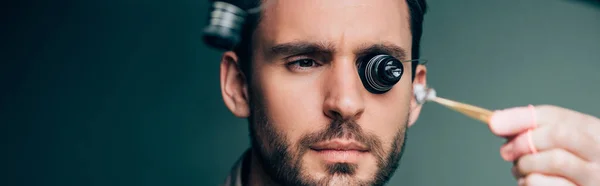 Selektiver Fokus des Uhrmachers in Brillenlupe mit Uhrenteil, Panoramaaufnahme — Stockfoto