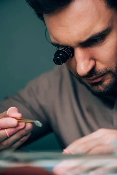 Selective focus of handsome clockmaker working with watch part at table — Stock Photo