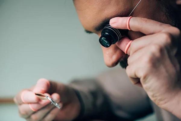 Vue latérale de l'horloger au bout des doigts en latex tenant loupe de lunettes et pièce de montre — Photo de stock