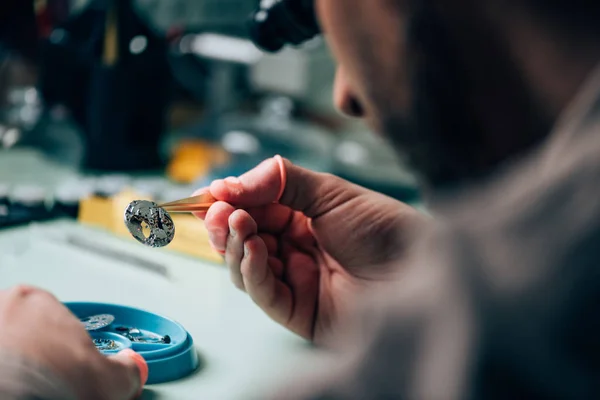 Selective focus of watchmaker holding watch part by tool tray on table — Stock Photo