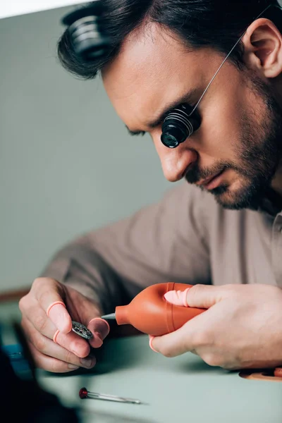 Seitenansicht des Uhrmachers in Brillenlupe, der mit Uhrenteil und Gebläse arbeitet — Stockfoto