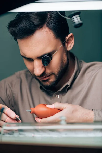 Selective focus of handsome watchmaker working with blower and watch part — Stock Photo