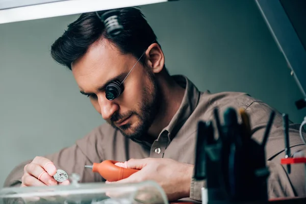 Selective focus of watchmaker working with watchpart and blower by equipment on table — Stock Photo