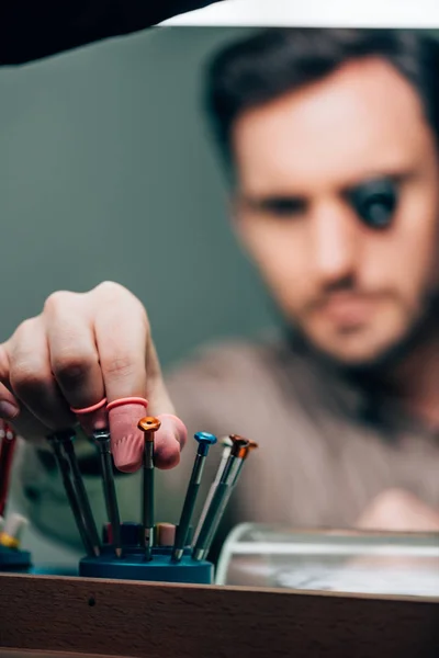 Selective focus of clockmaker in latex fingertips taking screwdriver while working at table — Stock Photo