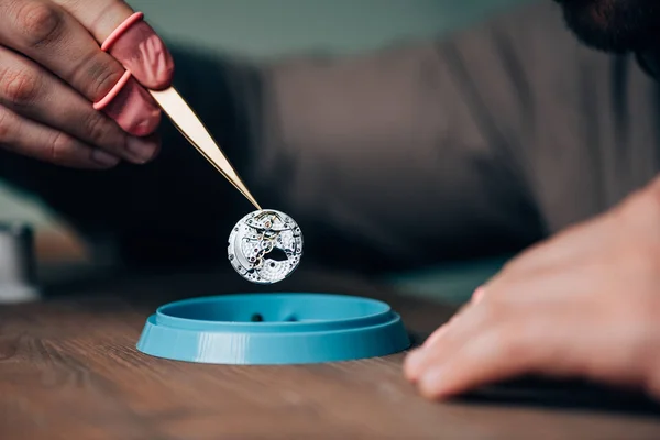 Cropped view of watchmaker holding watch part above tool tray on table — Stock Photo