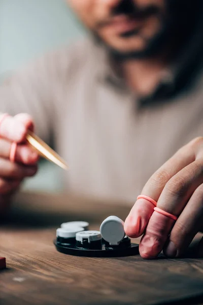 Вибірковий фокус годинникаря в латексних кінчиках пальців, що тримає пінцет та лоток для інструментів за столом — стокове фото