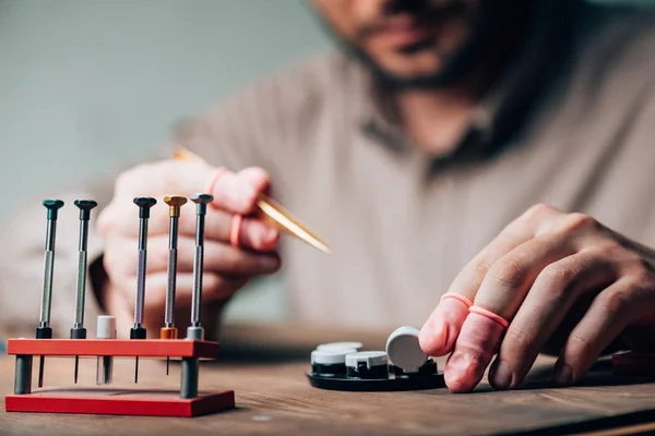 Cropped view of watchmaker holding tweezers by tool tray and screwdrivers on table — Stock Photo