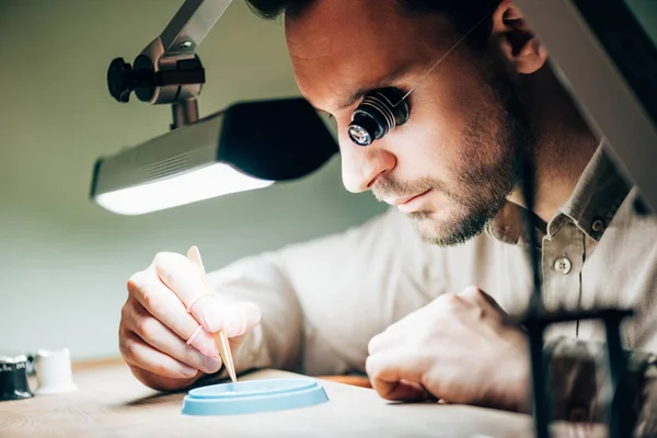 Side view of matchmaker with tweezers by tool tray and lamp on table — Stock Photo