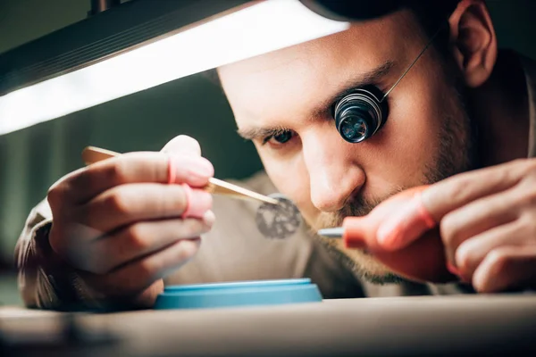 Selektiver Fokus des Uhrmachers, der mit Uhrteil und Gebläse durch Lampe auf dem Tisch arbeitet — Stockfoto