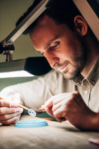 Side view of watchmaker using blower for cleaning watch part at table — Stock Photo