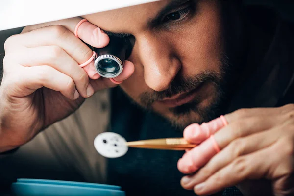 Selective focus of watchmaker holding eyeglass loupe and watch part by lamp — Stock Photo