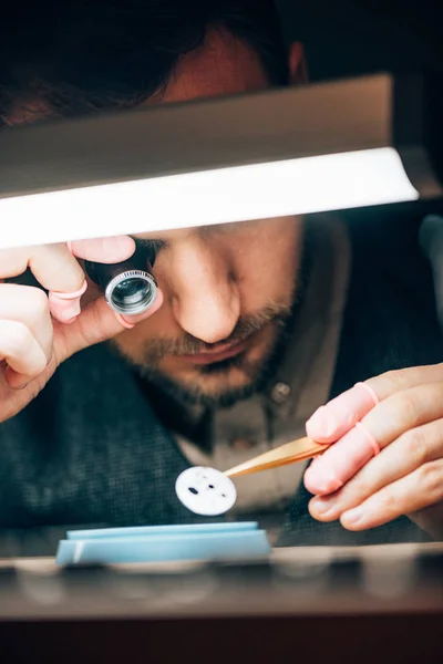 Focus selettivo dell'orologiaio che tiene la lente per occhiali e guarda la parte al tavolo di lavoro — Foto stock