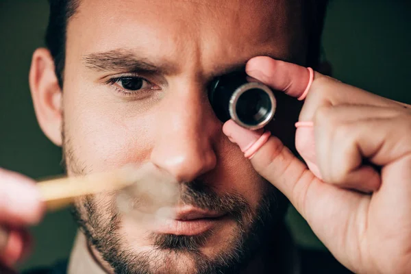 Selective focus of handsome watchmaker holding eyeglass loupe and watch part — Stock Photo