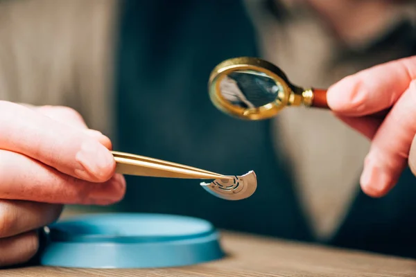 Cropped view of clockmaker working with magnifying glass and watch detail by tool tray on table — Stock Photo