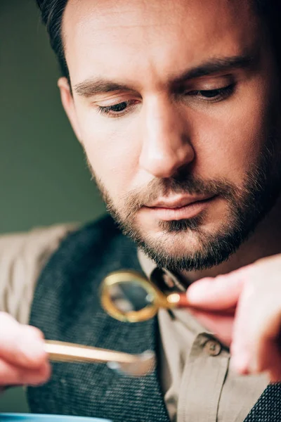 Selective focus of handsome watchmaker holding magnifying glass and watch part — Stock Photo