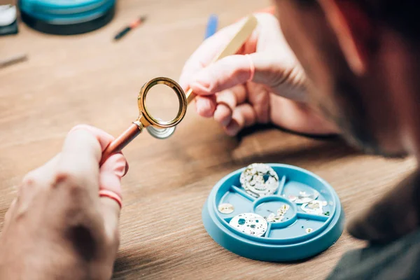 Mise au point sélective de l'horloger en utilisant la loupe par plateau à outils avec des pièces de montre sur la table — Photo de stock