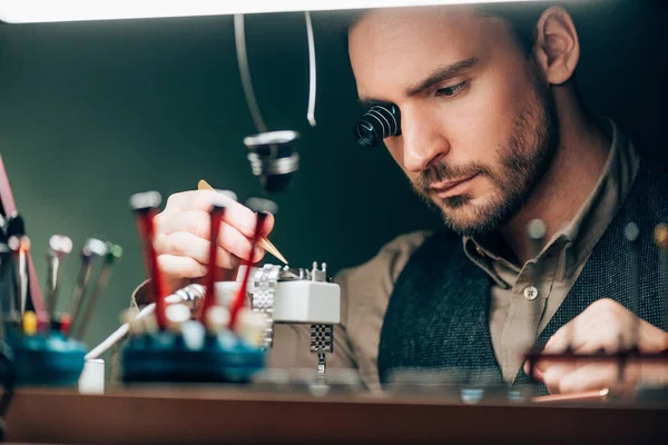 Selective focus of watchmaker repairing wristwatch at table — Stock Photo