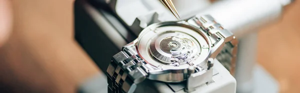 Panoramic shot of wristwatch on watch tester by tweezers on table — Stock Photo