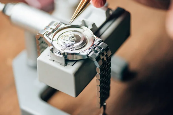 Cropped view of watchmaker working with tweezers and wristwatches on movement holder — Stock Photo